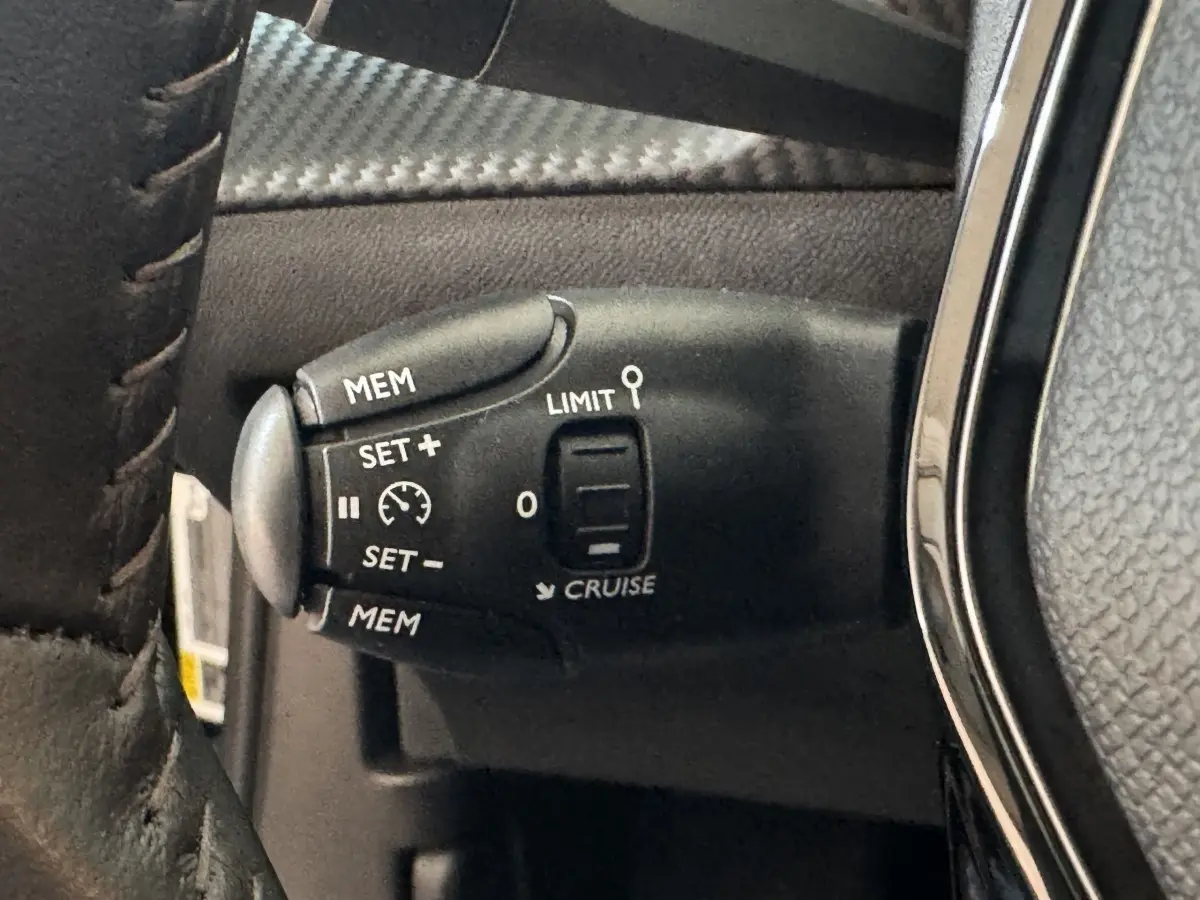 Gros plan sur la commande de régulateur de vitesse noire avec marquages blancs, sur le volant cuir d’un Peugeot 2008 noir.