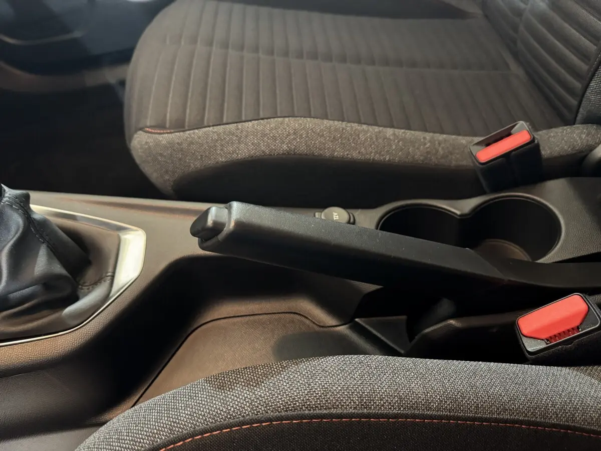 Vue rapprochée de la console centrale intérieure du Peugeot 2008 2022 noire, avec frein à main manuel et sièges tissu gris.