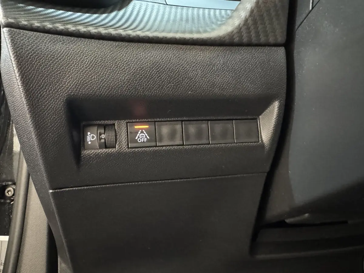 Vue rapprochée du tableau de bord côté conducteur de la Peugeot 2008 noire, avec commandes d'éclairage et d'assistance activée.