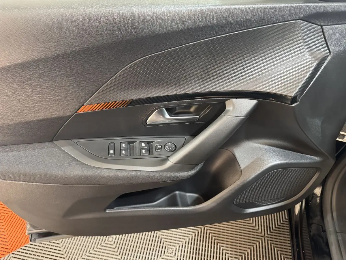 Vue rapprochée de la porte côté conducteur du Peugeot 2008 noir, avec insert décoratif carbone et commandes électriques.