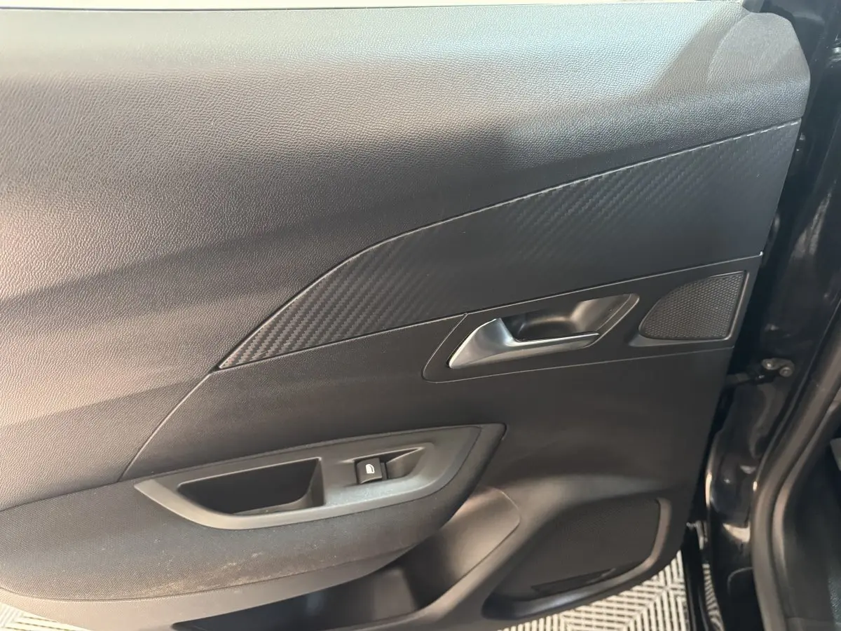 Vue intérieure côté droit de la porte avant noire du Peugeot 2008 avec poignée argentée et habillage effet carbone.