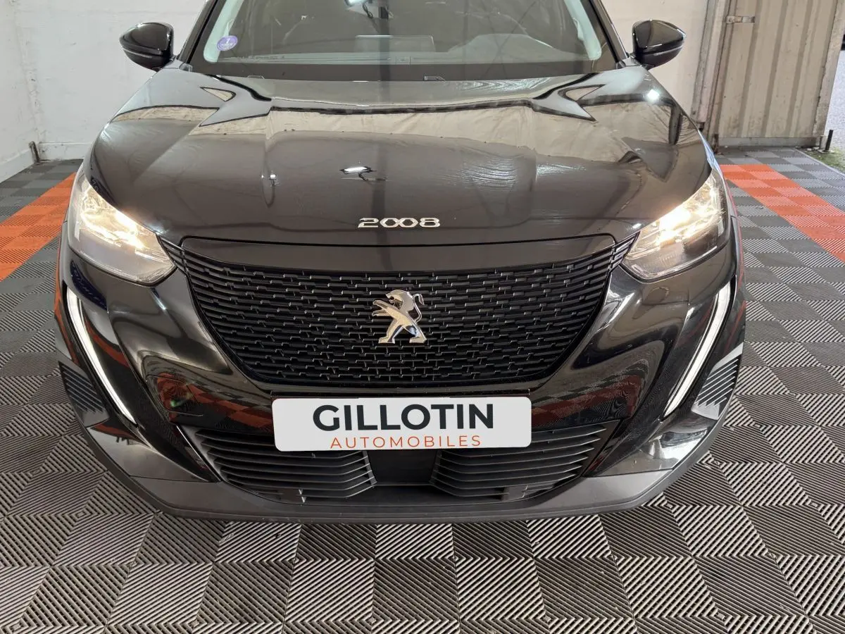 Vue avant rapprochée d’une Peugeot 2008 noire avec calandre distinctive et phares allumés dans un showroom.