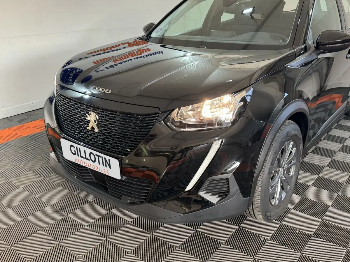Vue 3/4 avant droit d'un Peugeot 2008 noir avec calandre noire et phares allumés dans un showroom.