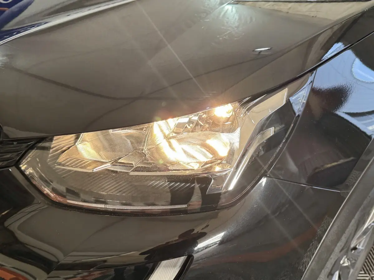 Gros plan sur le phare avant droit allumé d’un Peugeot 2008 noir, soulignant les lignes modernes du capot.