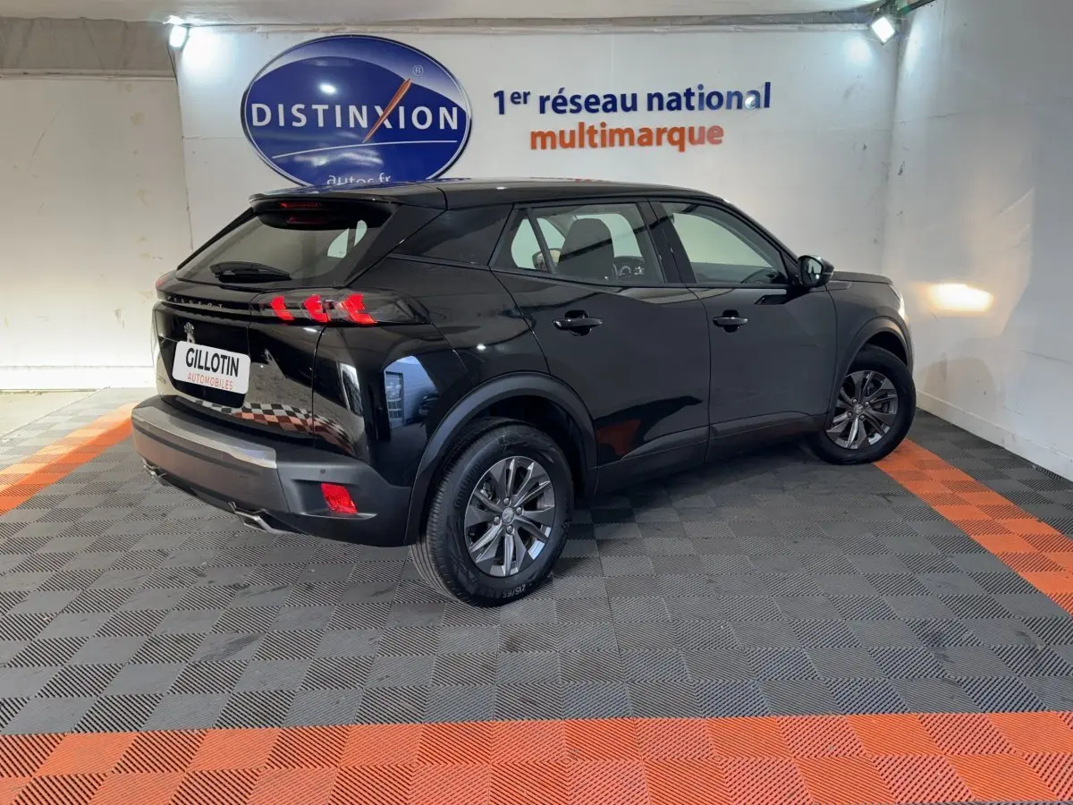 Vue 3/4 arrière droite d'un Peugeot 2008 noir 2022 dans un showroom avec sol gris et orange.