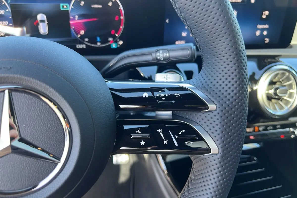 Gros plan sur le volant cuir perforé de la Mercedes Classe A 200D 2026, avec commandes multifonctions et tableau de bord numérique.