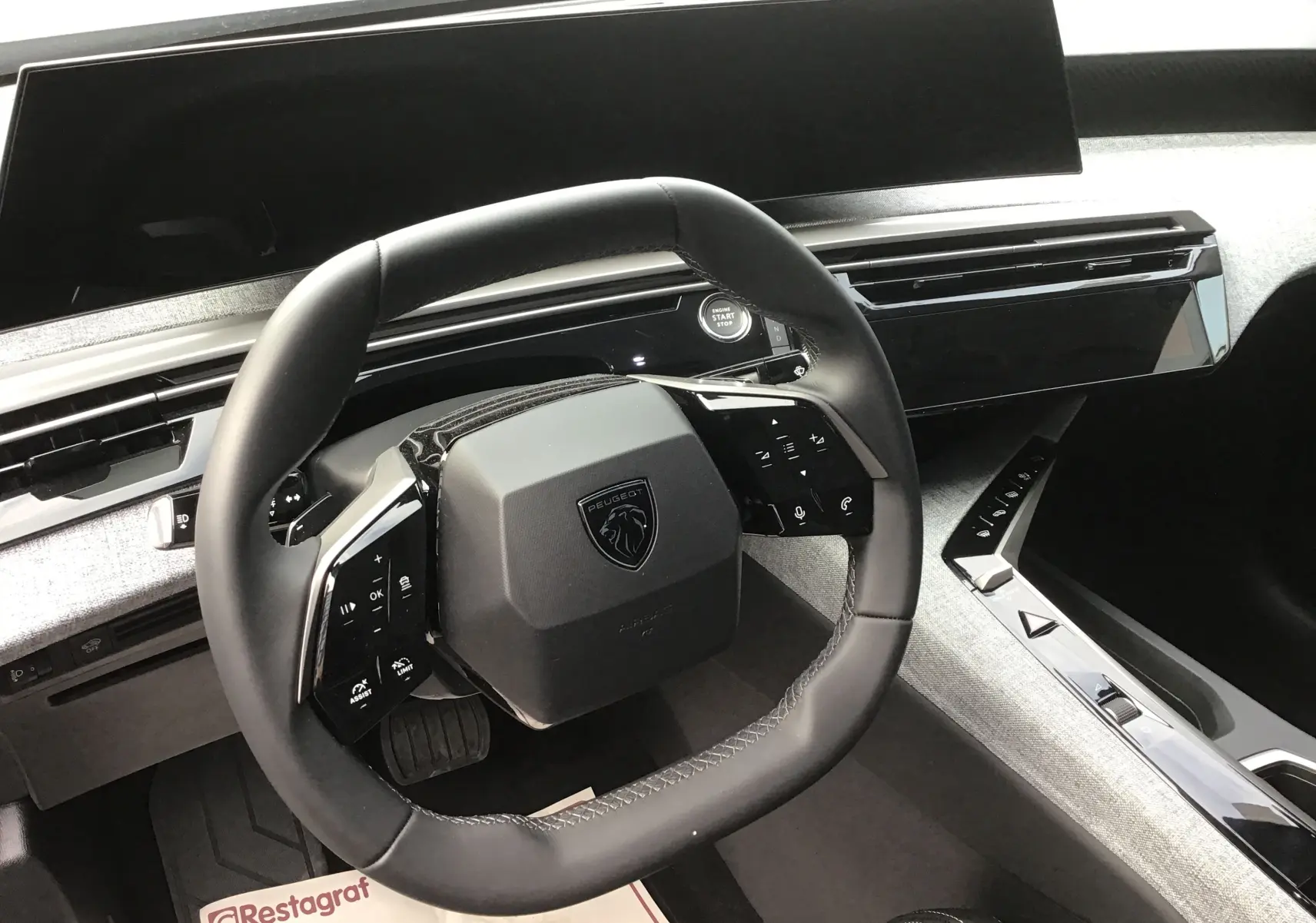 Vue intérieure centrée sur le volant carré du Peugeot 3008 2026, avec tableau de bord numérique et finition gris clair.