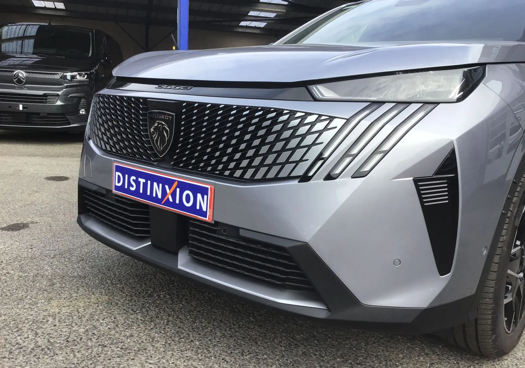 Vue avant droite du Peugeot 3008 1.2 Hybrid gris Artense avec calandre noire à motif losange et phares effilés.
