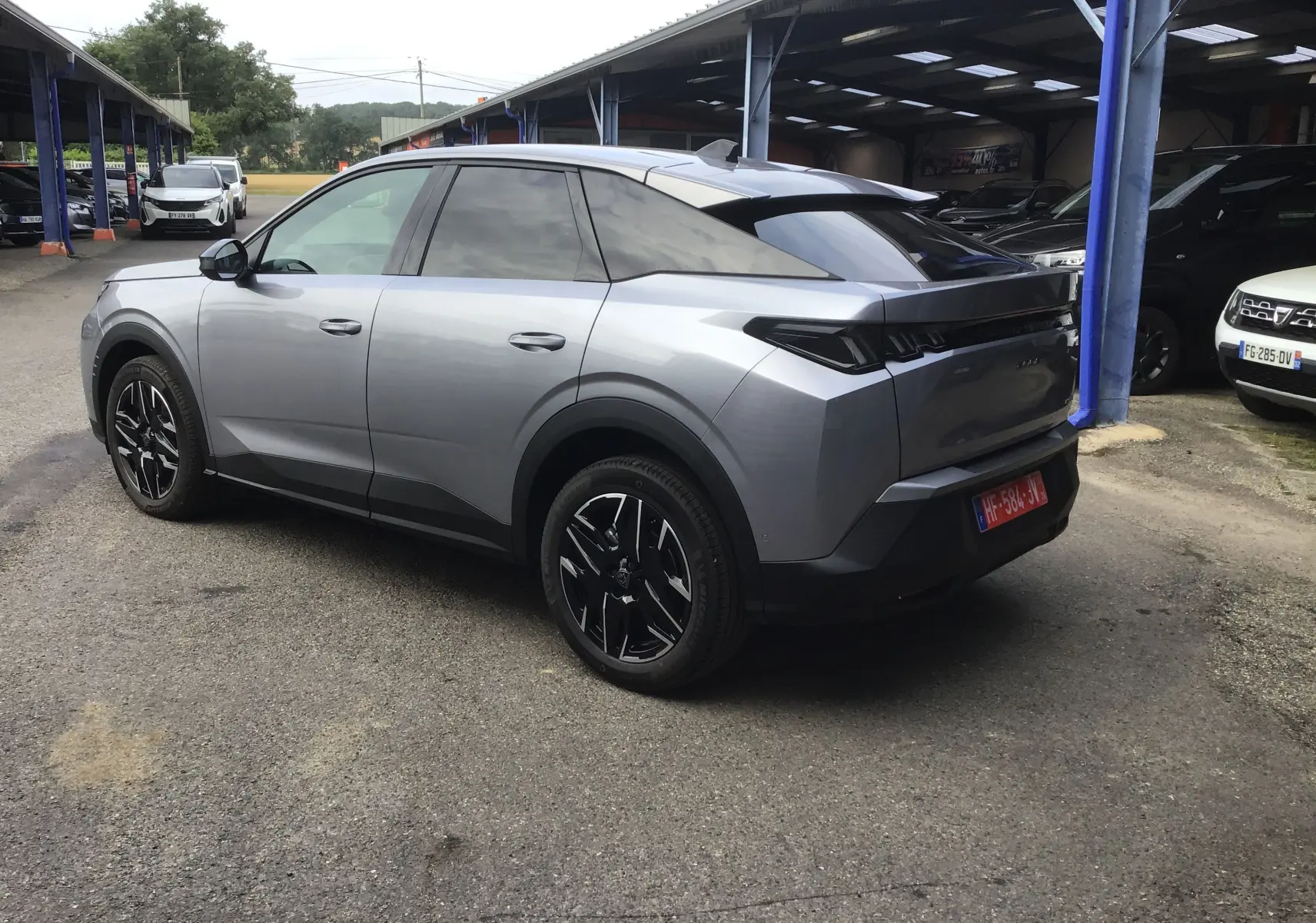 Vue 3/4 arrière droite d’un Peugeot 3008 gris Artense 2026 avec jantes noires et vitres teintées, stationné sous abri.