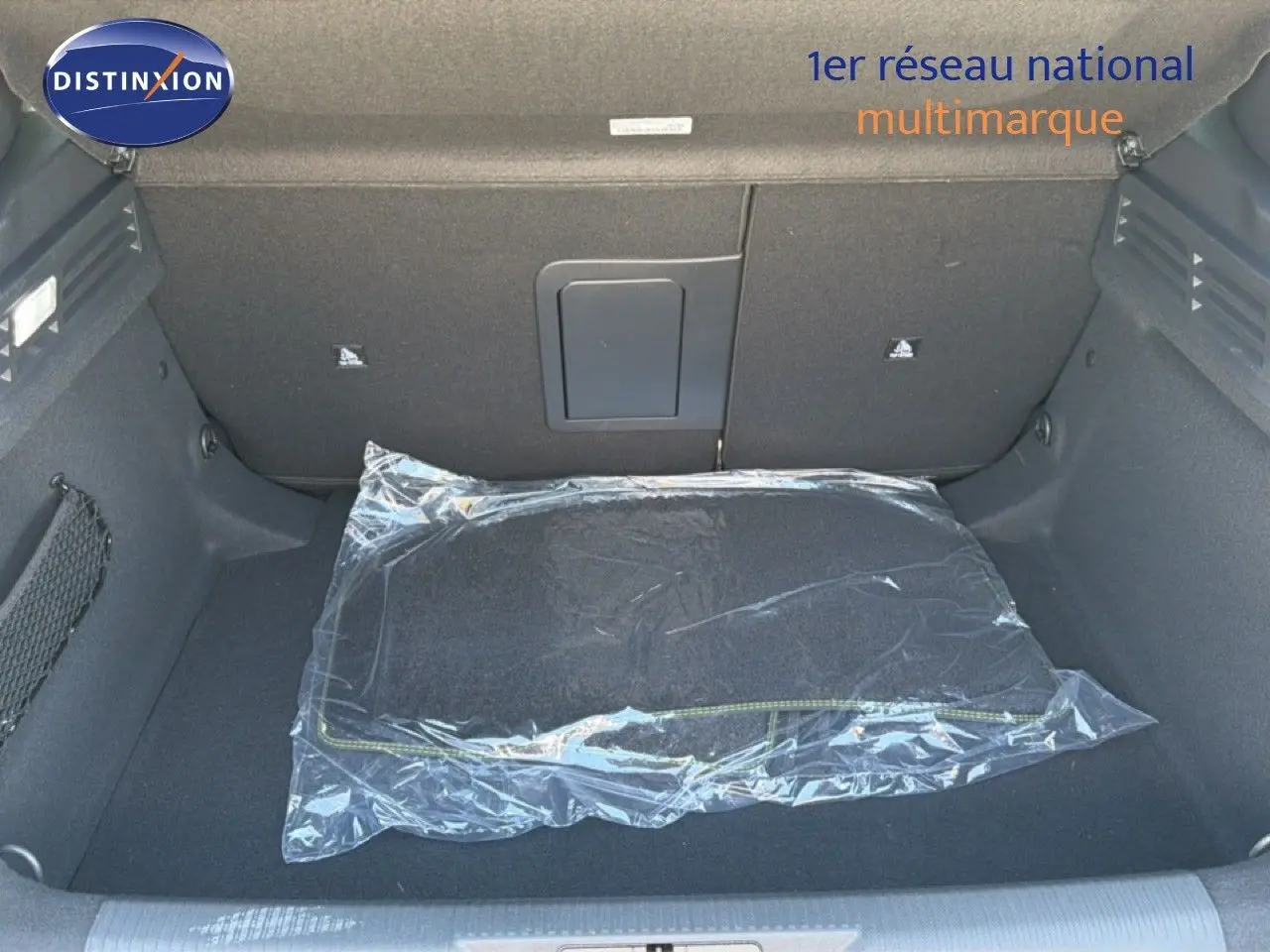 Coffre ouvert de la Peugeot 308 Hybrid 145ch GT noir perle métal, montrant un tapis de sol emballé en plastique.