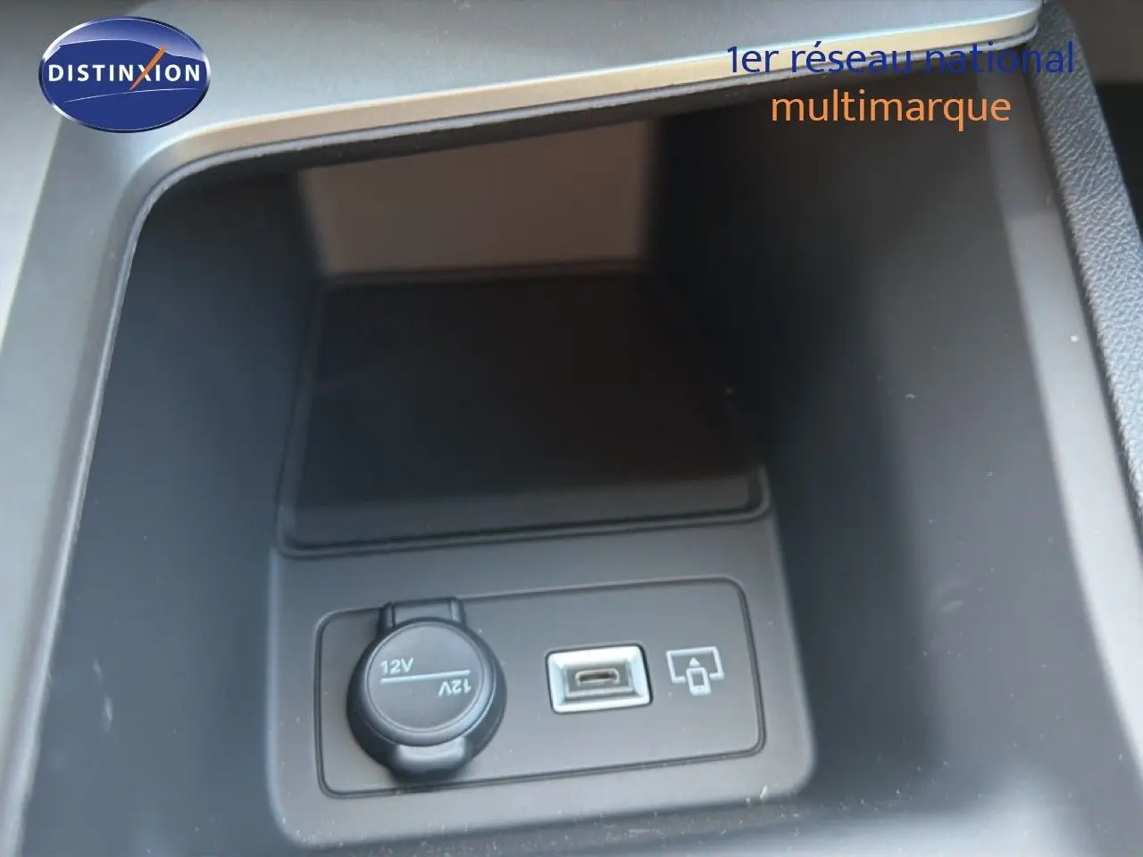 Gros plan sur la prise 12V et port USB dans le rangement central d'une Peugeot 308 Hybrid 145ch GT noir perle métal.