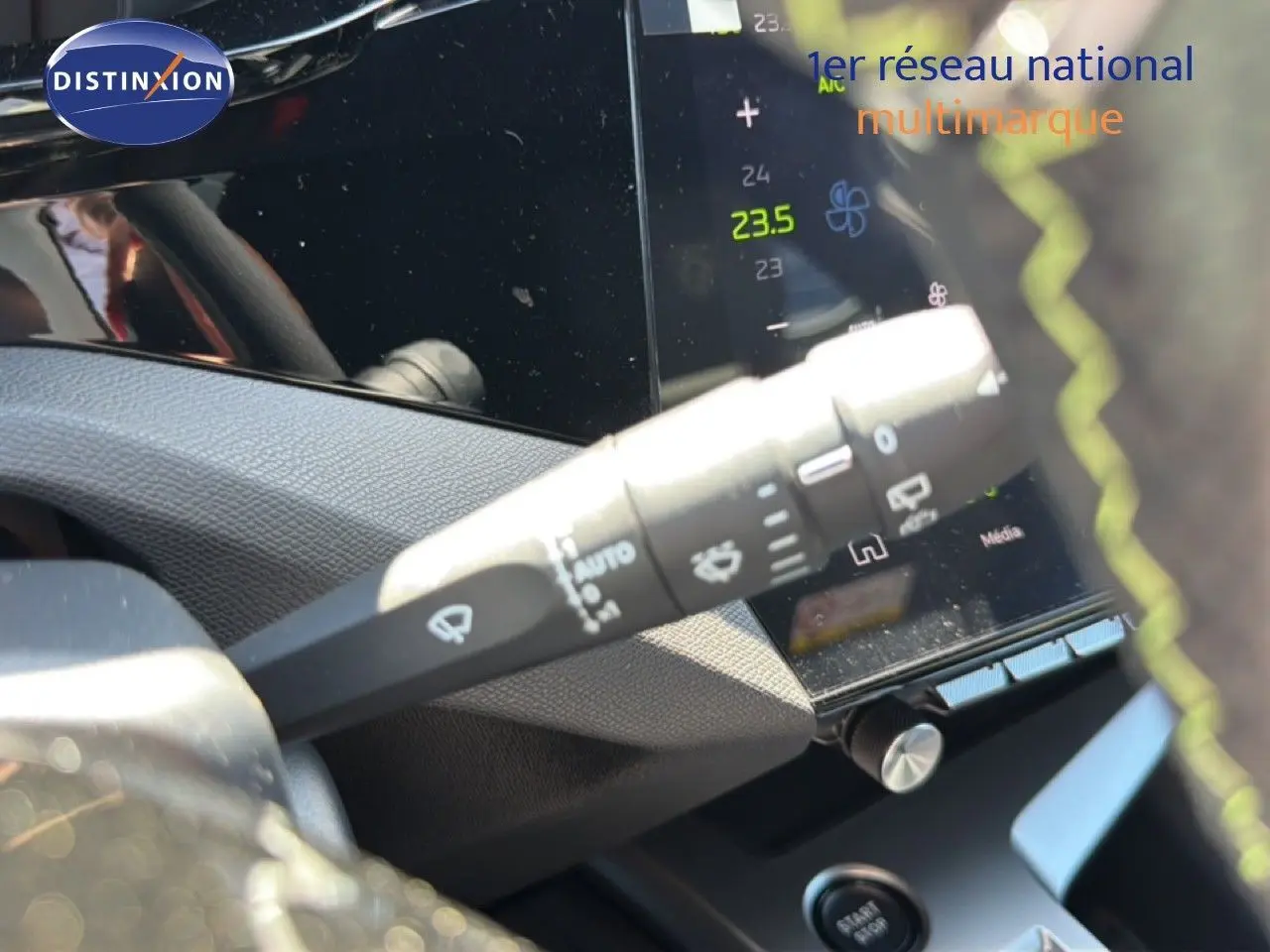 Gros plan sur la commande d’essuie-glace à gauche du volant d’une Peugeot 308 Hybrid noire, avec écran tactile en arrière-plan.