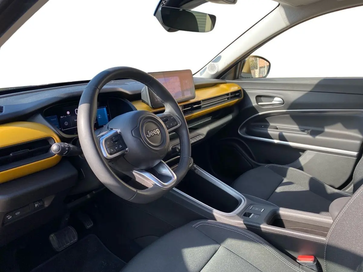 Intérieur du Jeep Avenger électrique 2023, vue côté conducteur, tableau de bord noir et jaune avec écran tactile central.