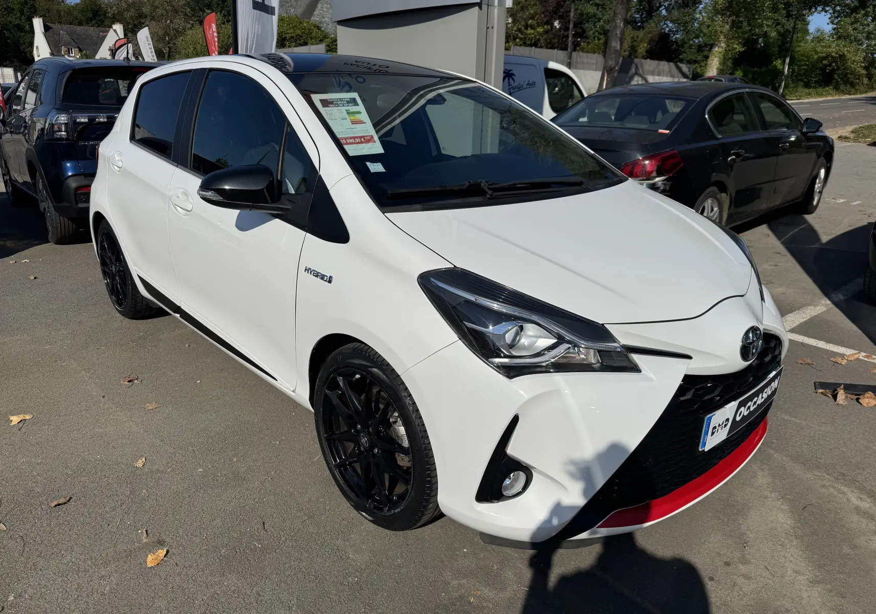 Toyota Yaris Hybride 100CH GR SPORT blanc vue 3/4 avant droit avec jantes noires et détails rouges sur le pare-chocs.