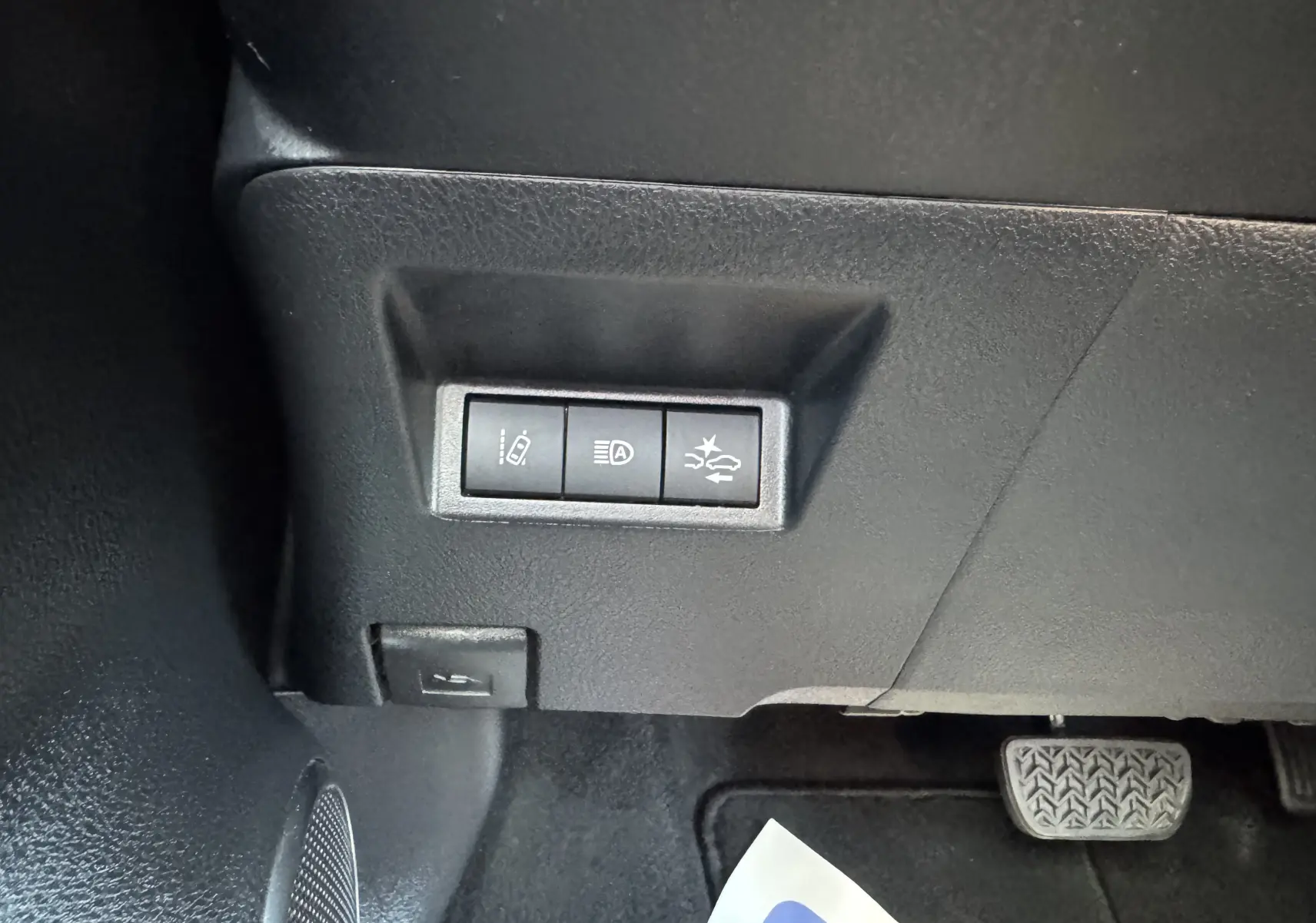 Gros plan sur les commandes de sécurité sous le tableau de bord d'une Toyota Yaris Hybride blanche, version GR Sport 2020.