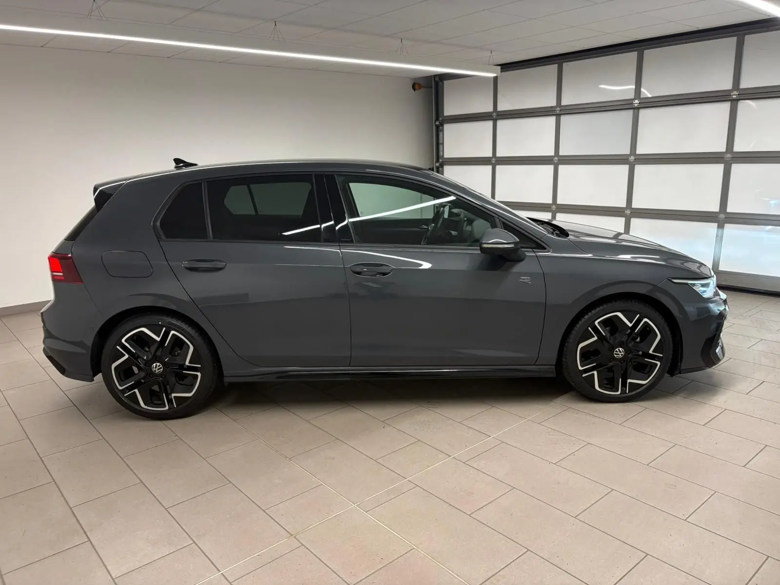 Profil droit d'une Volkswagen Golf 1.5 eTSI 150 DSG7 R-Line Edition gris dauphin, avec jantes noires et détails sportifs.