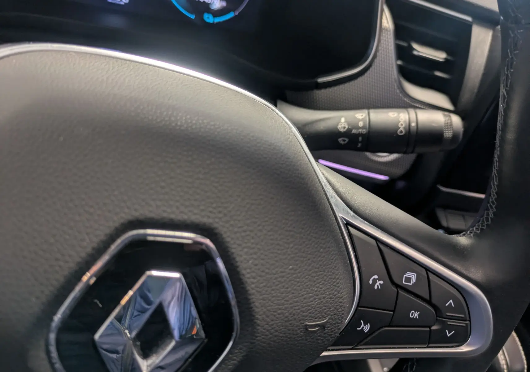 Gros plan sur le volant noir du Renault Arkana 2023, avec commandes multifonctions et tableau de bord numérique en arrière-plan.