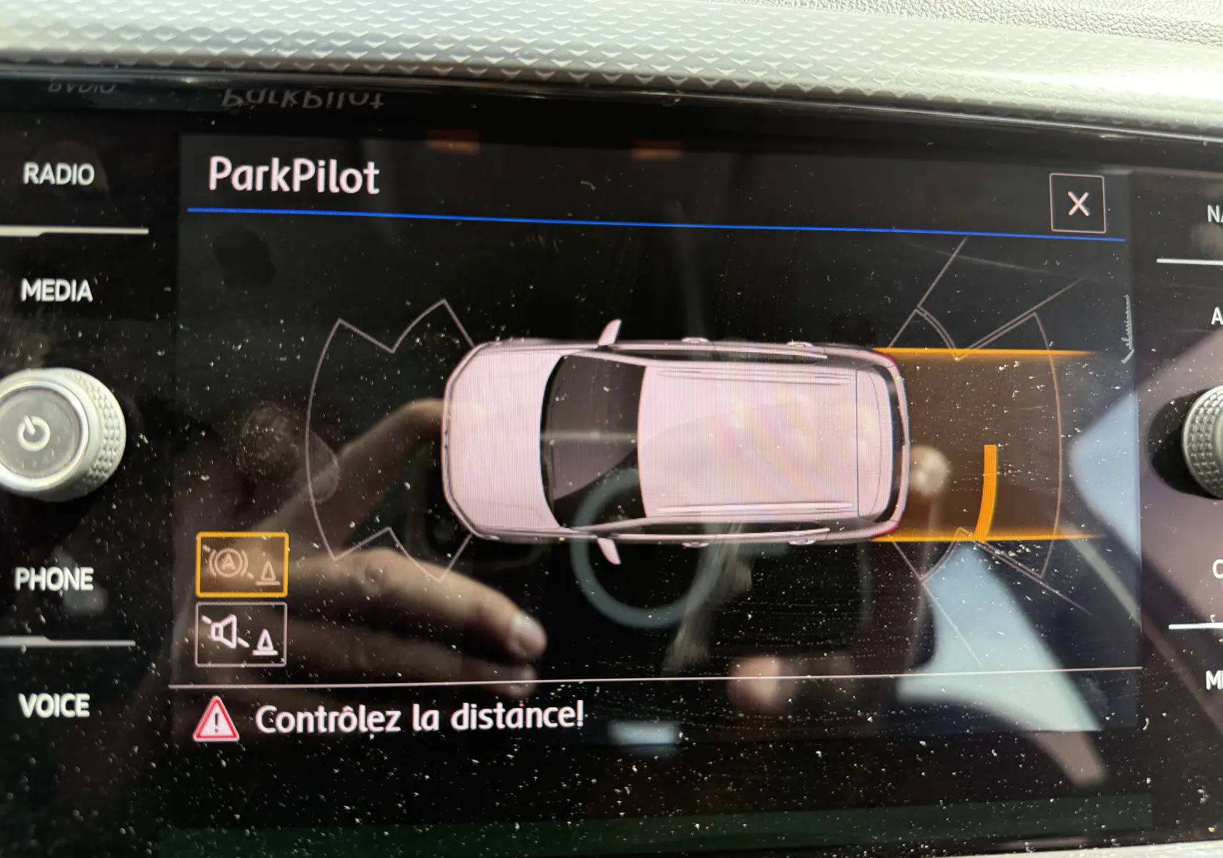 Affichage du système ParkPilot sur écran multimédia, vue de dessus du Volkswagen T-Cross gris indiquant une alerte de proximité arrière.