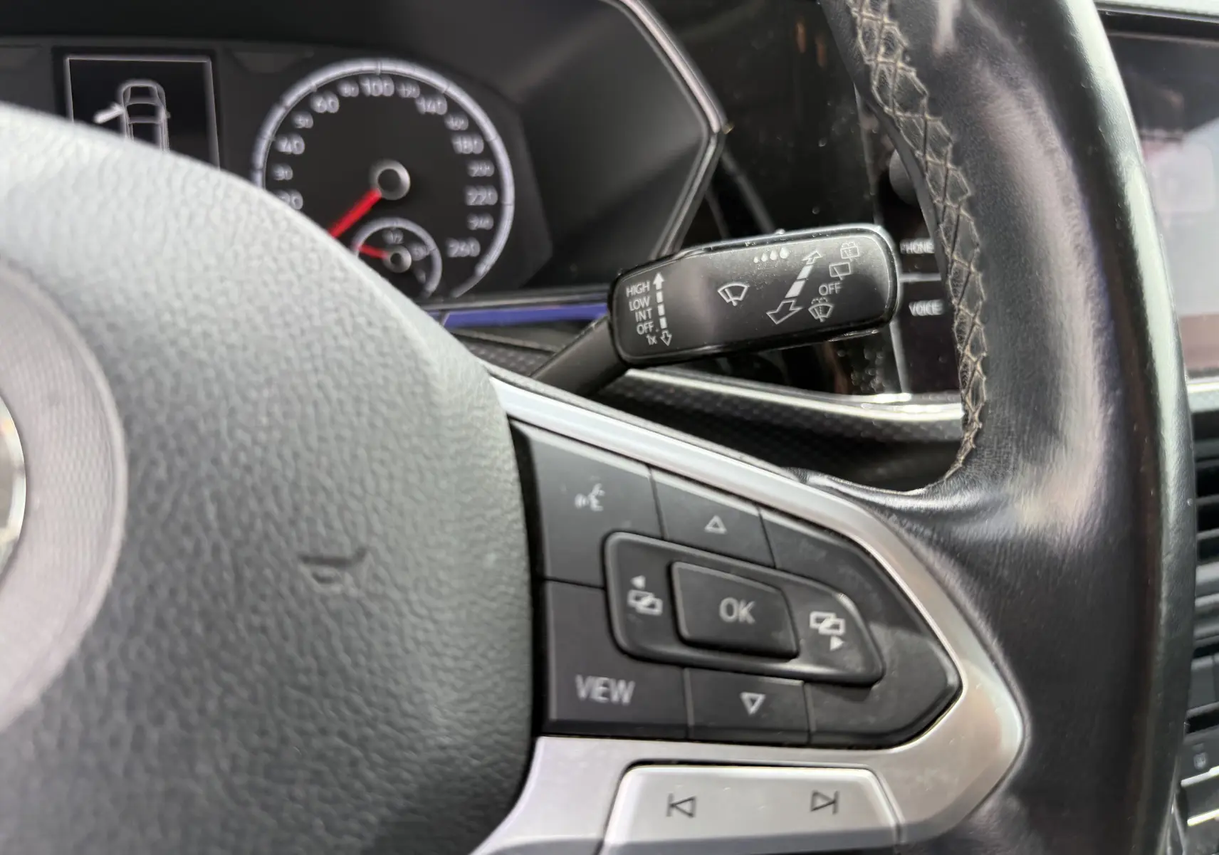 Gros plan sur le volant côté gauche du Volkswagen T-Cross gris 2019 avec commandes intégrées et manette d’essuie-glace visible.