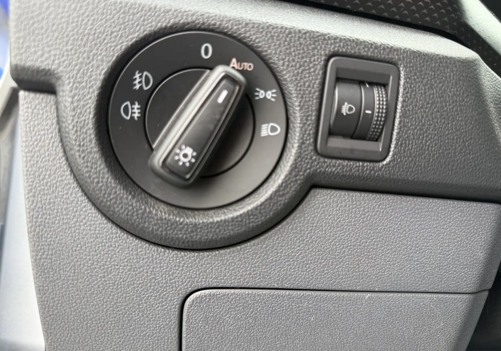 Gros plan sur le sélecteur de phares noir et la molette de réglage d’intensité lumineuse dans l’habitacle gris du Volkswagen T-Cross 2019.