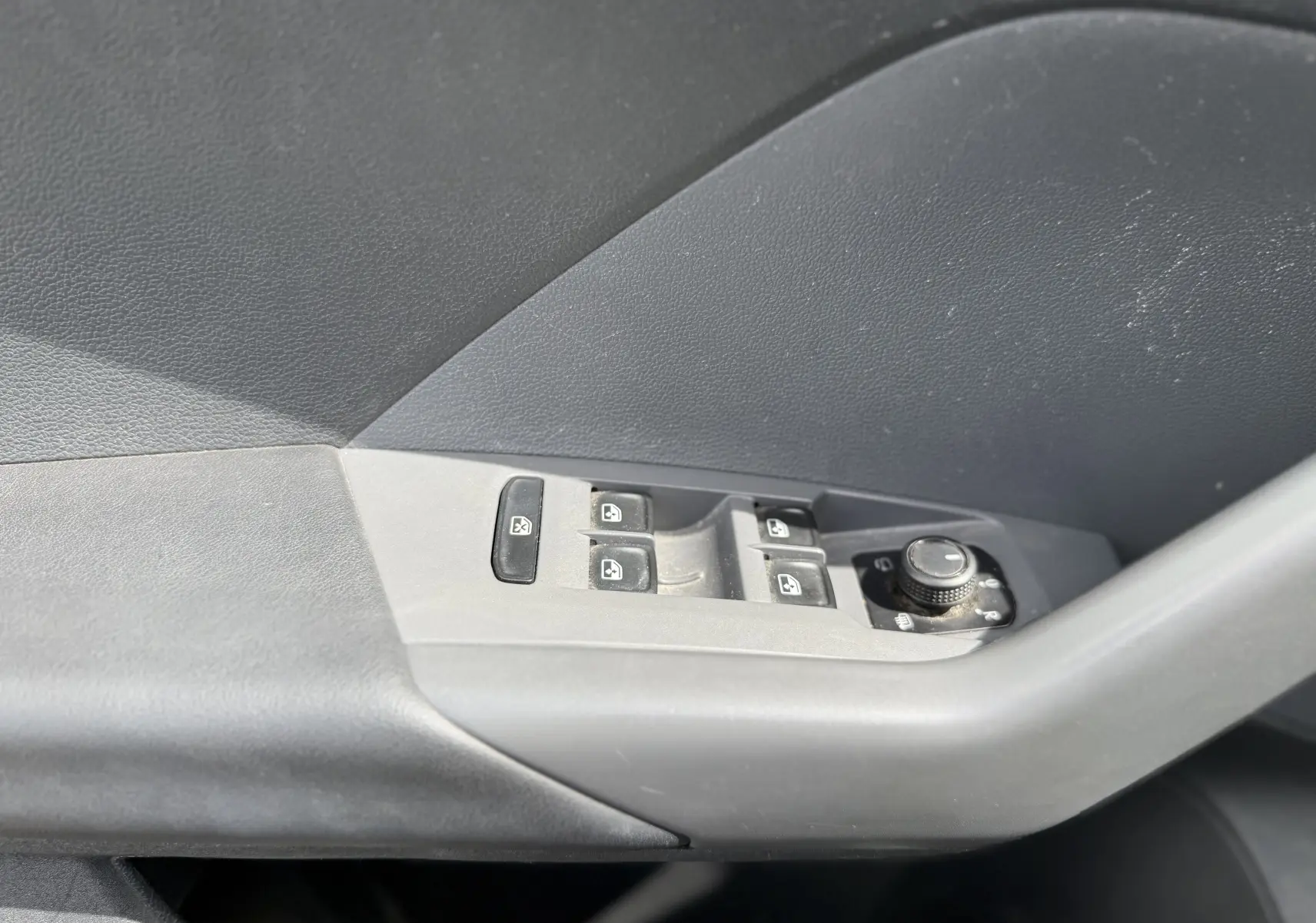 Gros plan sur la commande des vitres électriques et réglage des rétroviseurs côté conducteur d’un Volkswagen T-Cross gris 2019.