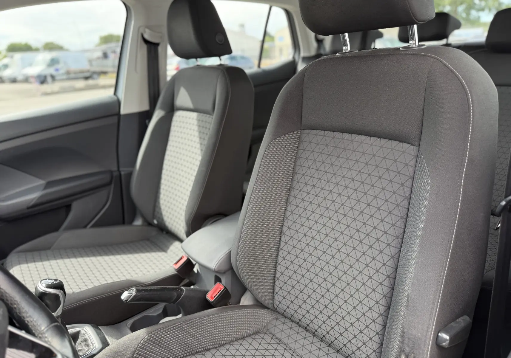 Vue intérieure côté gauche du Volkswagen T-Cross gris 2019, montrant les sièges avant en tissu et la boîte manuelle.