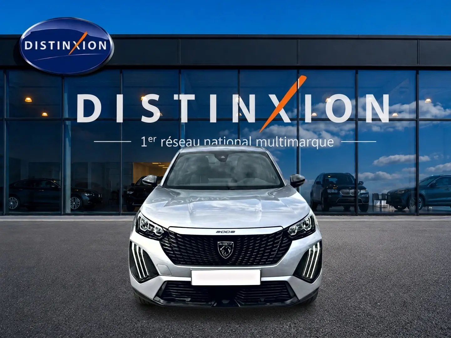 Vue avant d'un Peugeot 2008 gris 2025 avec calandre noire et feux LED distinctifs, devant une vitrine Distinxion.