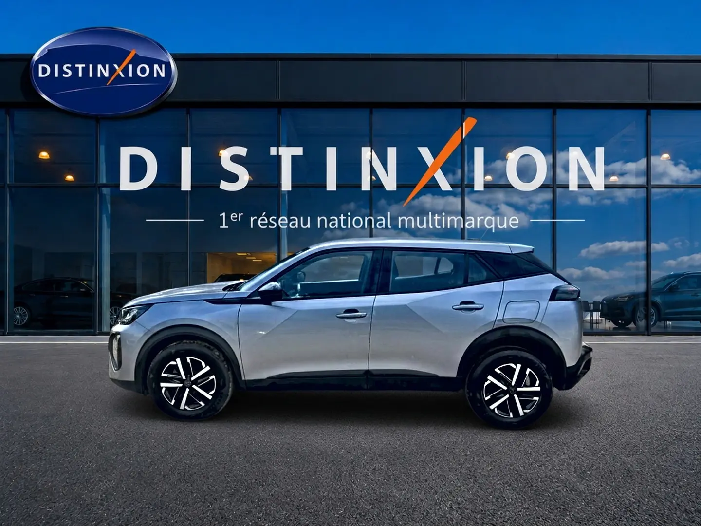 Peugeot 2008 gris en profil droit, avec jantes noires et toit noir, devant une vitrine Distinxion.