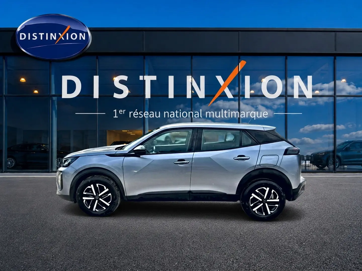 Profil côté gauche du Peugeot 2008 gris 2025 avec jantes noires et toit contrasté blanc devant une vitrine Distinxion.