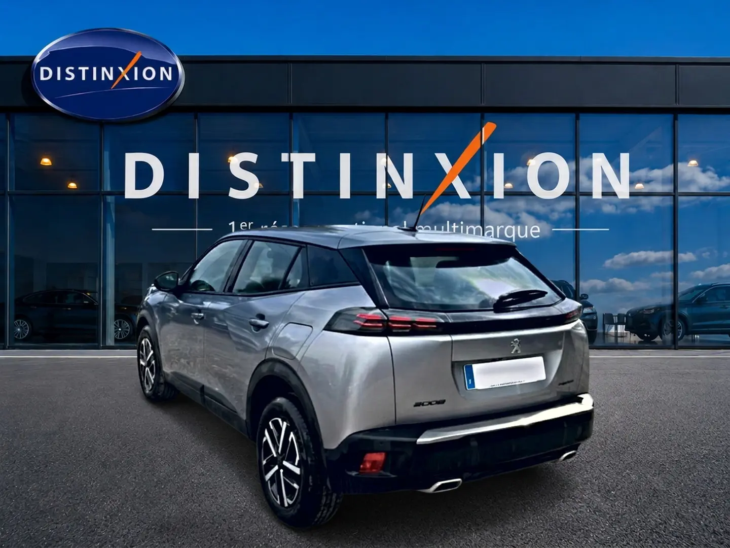 Peugeot 2008 gris en 3/4 arrière droit, avec feux arrière LED et becquet noir, devant une vitrine Distinxion.