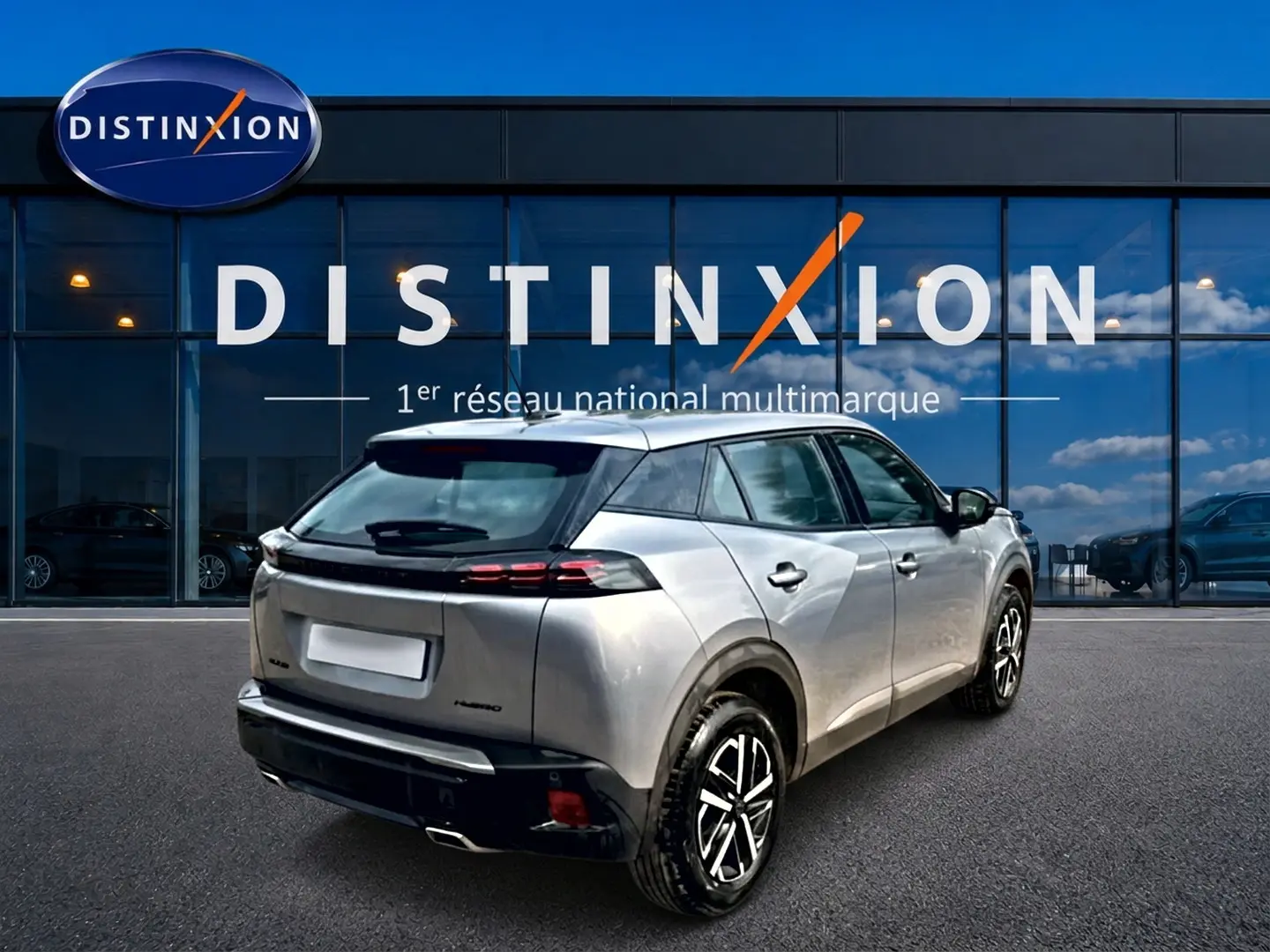 Peugeot 2008 gris en 3/4 arrière droit, avec becquet et feux arrière LED, devant une vitrine Distinxion.