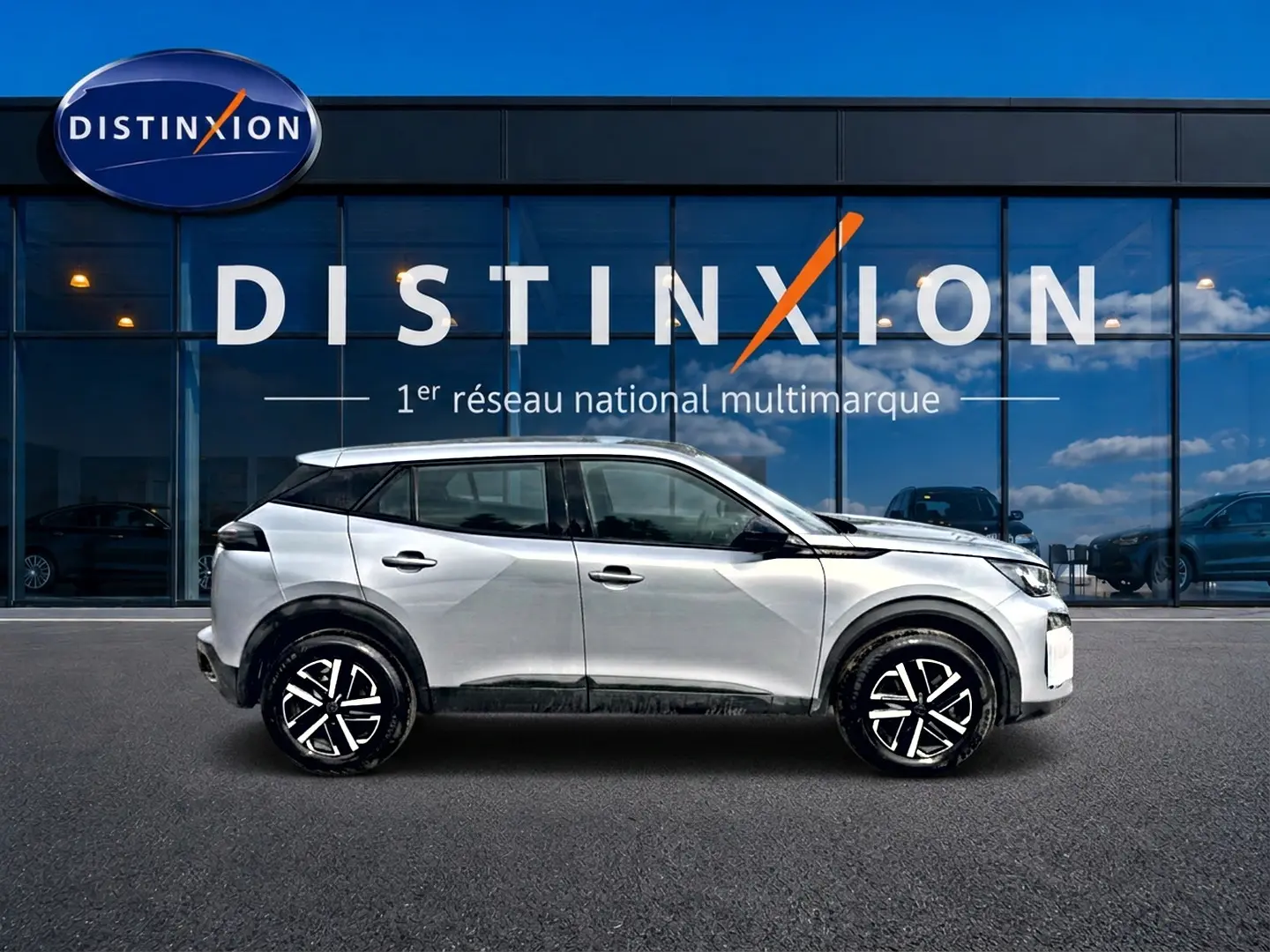 Profil droit du Peugeot 2008 gris 2025 avec jantes noires et toit noir devant une vitrine Distinxion.