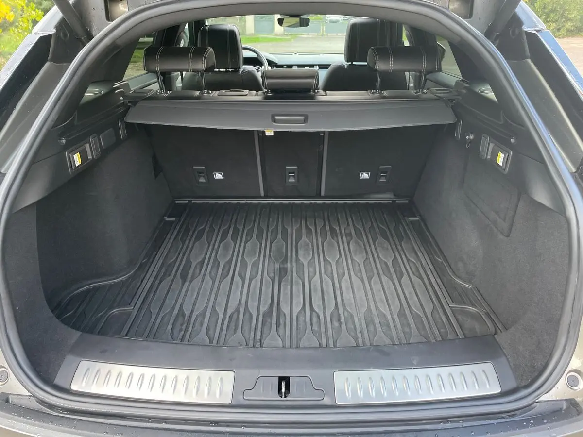 Coffre ouvert d’un Range Rover Velar gris 2019, montrant un tapis de coffre en caoutchouc et banquette arrière en cuir noir.