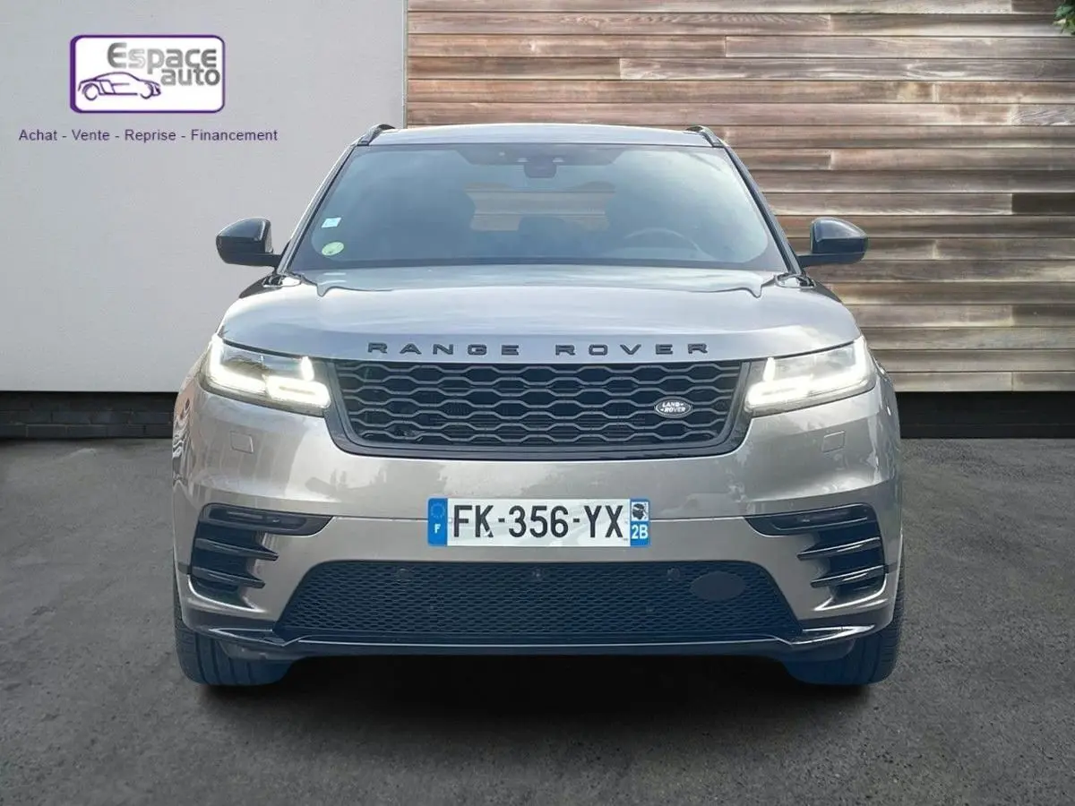 Vue frontale d'un Range Rover Velar gris 2019 avec calandre noire et phares LED allumés sur fond urbain.