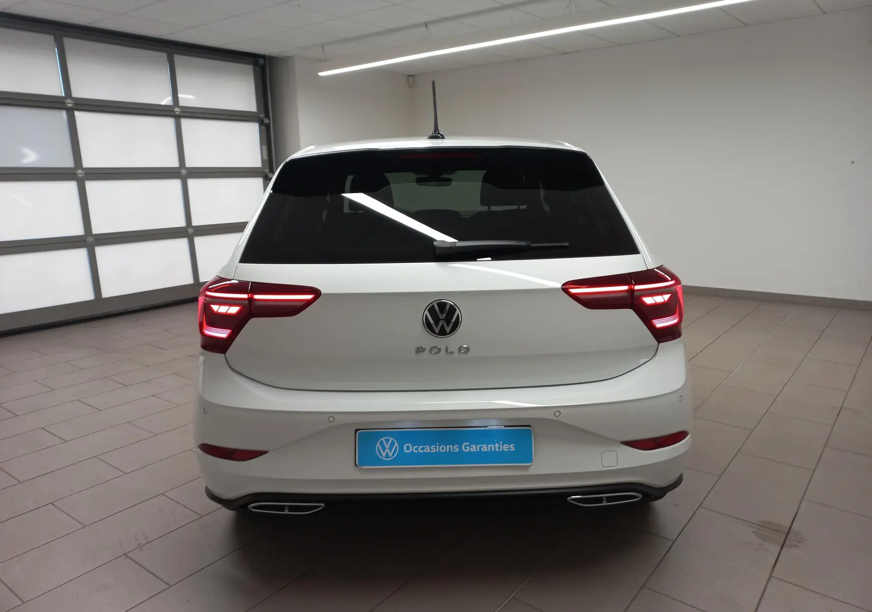 Vue arrière d'une Volkswagen Polo blanche avec feux allumés et vitres arrière surteintées dans un garage.