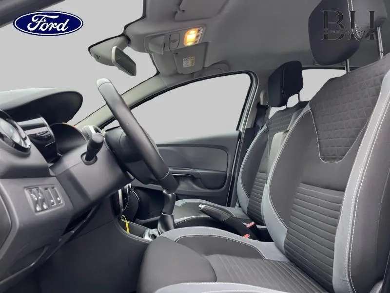 Vue intérieure côté conducteur de la Renault Clio gris Platine 2016, avec sièges tissu noir et volant cuir.