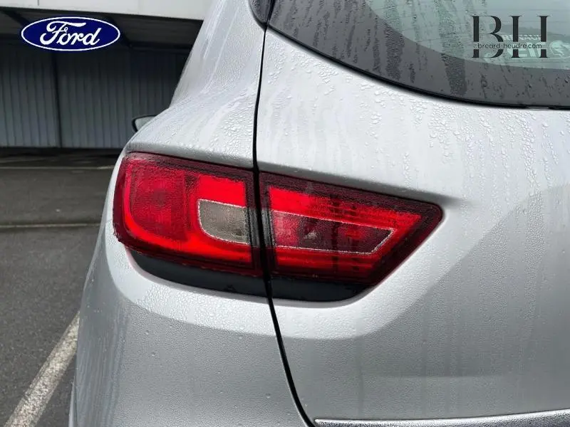 Gros plan sur le feu arrière droit d'une Renault Clio gris platine 2016, avec gouttes d'eau sur la carrosserie.