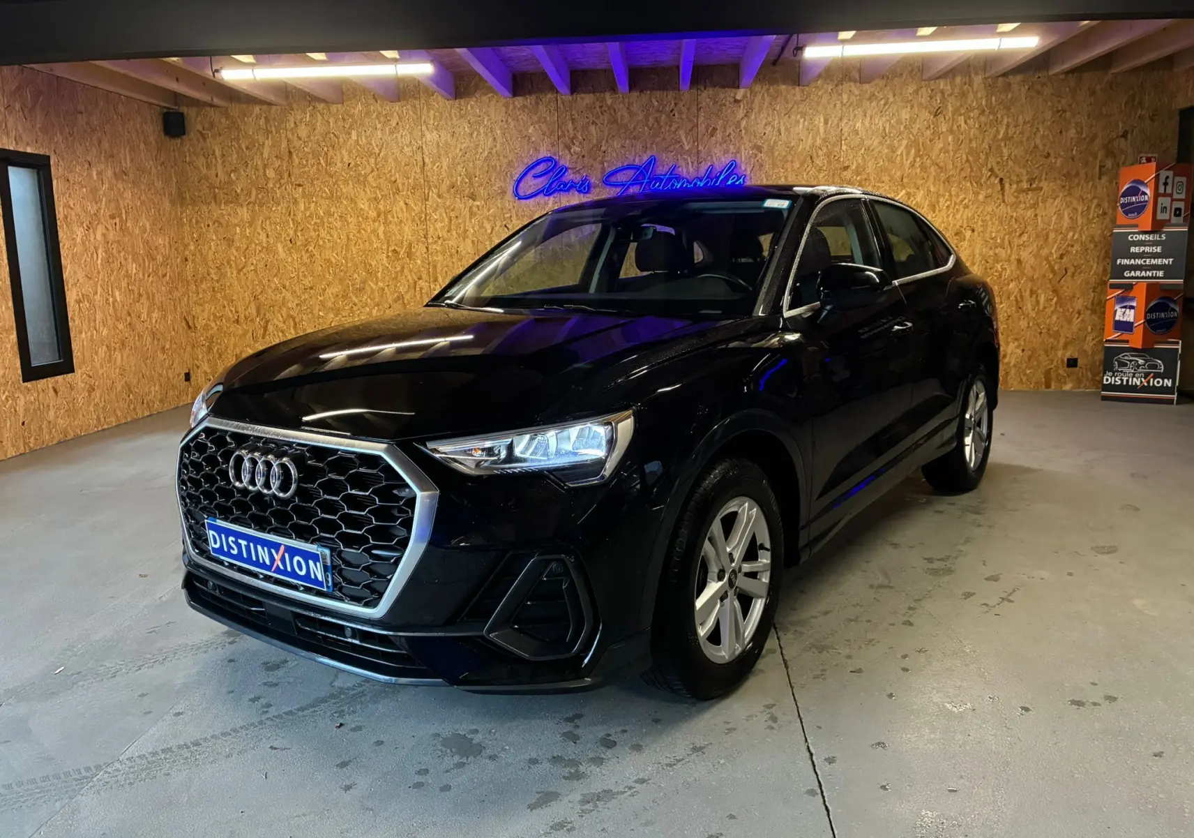 Audi Q3 Sportback noir vue 3/4 avant droit en intérieur, avec calandre hexagonale et jantes alu visibles.