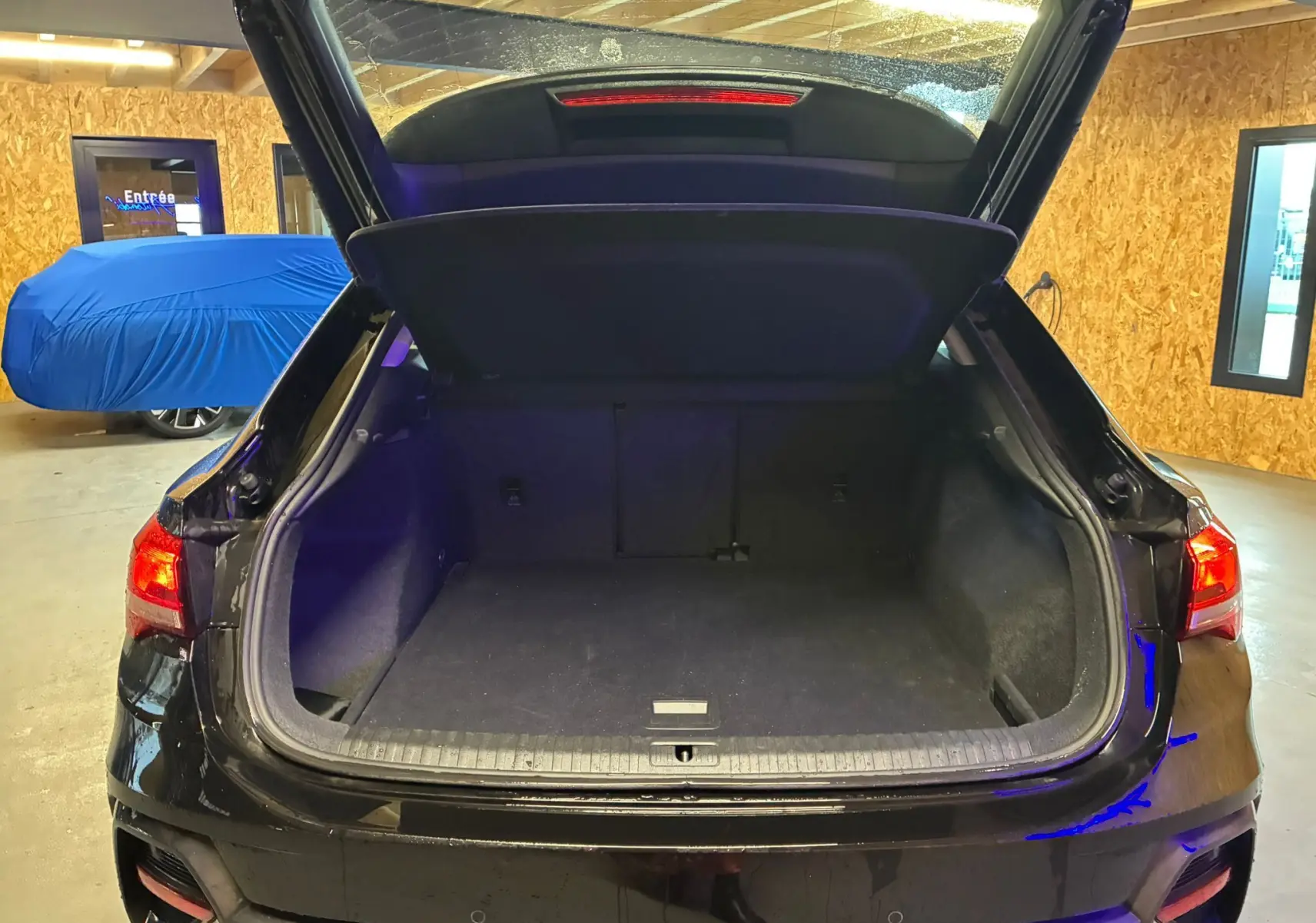 Vue arrière d'un Audi Q3 Sportback noir 2022 avec coffre ouvert, montrant l'espace de chargement vide en intérieur garage.