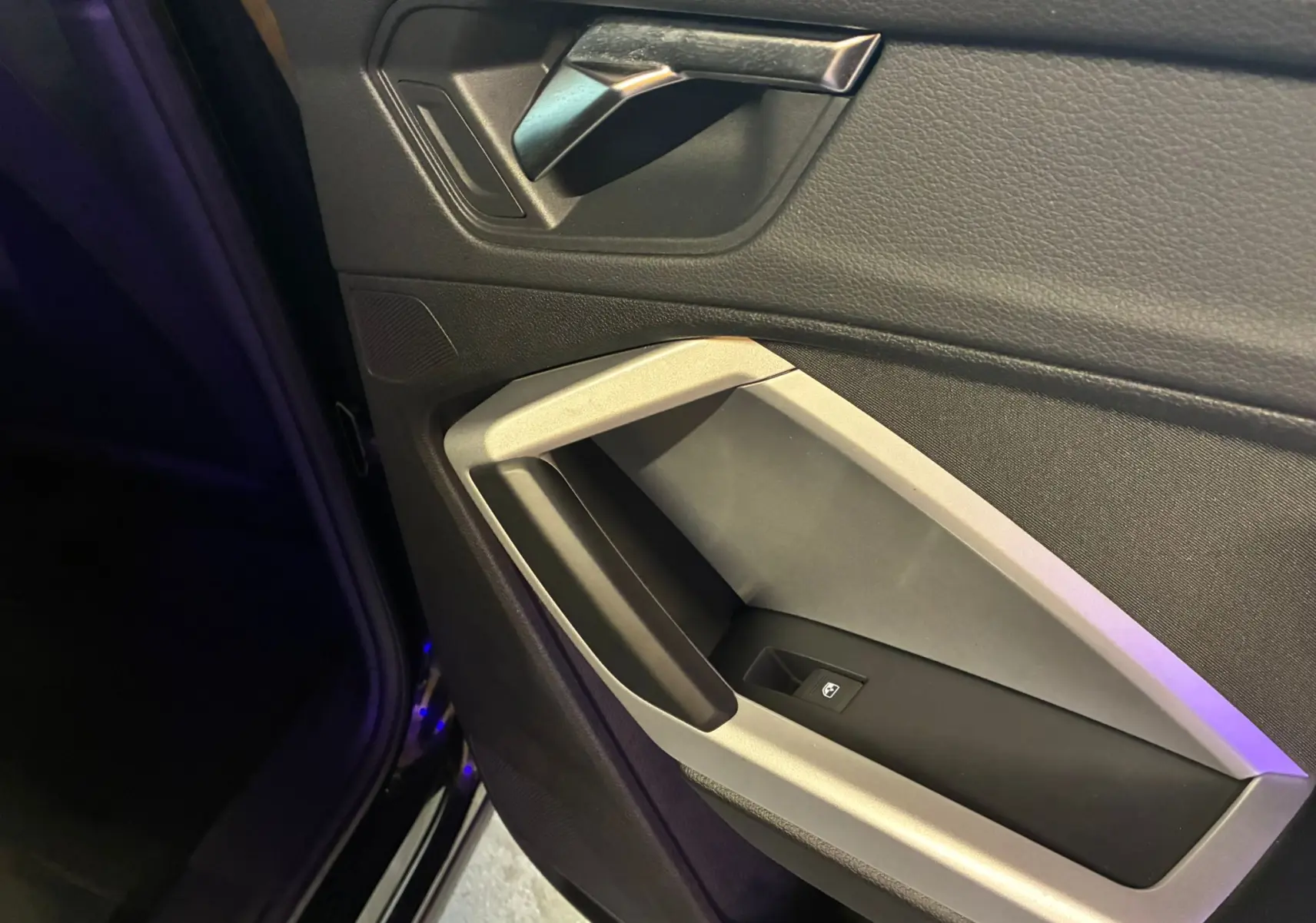 Gros plan sur la poignée intérieure et la commande de vitre côté gauche d’un Audi Q3 Sportback noir 2022.