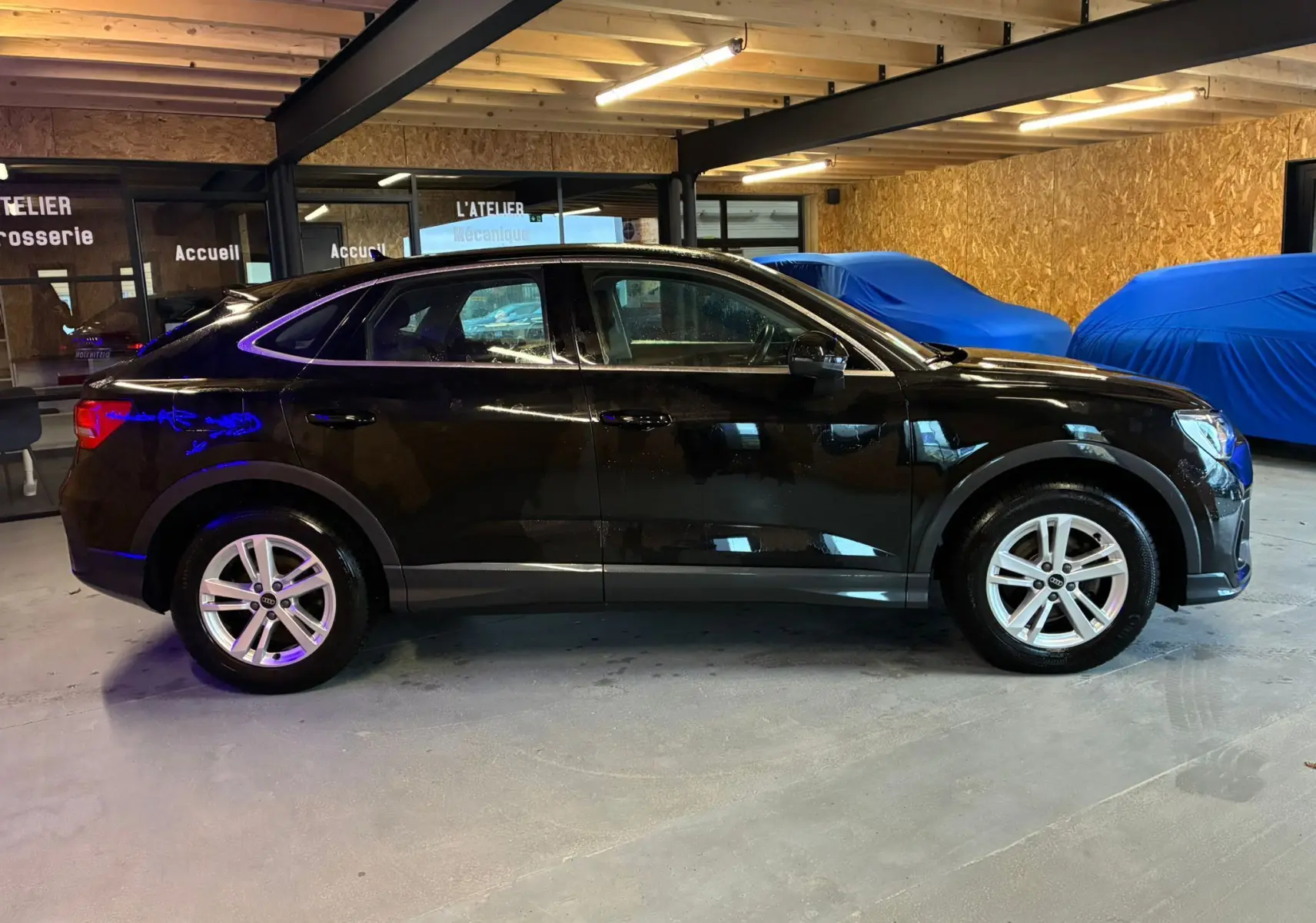 Audi Q3 Sportback noir vue de profil côté gauche dans un garage avec jantes alu et reflets lumineux.