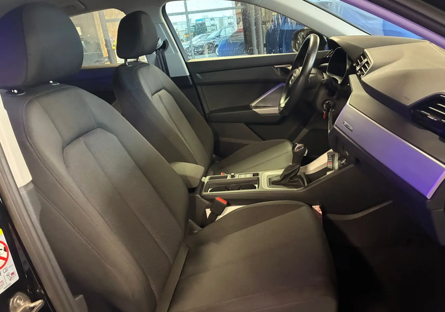 Vue intérieure côté conducteur de l'Audi Q3 Sportback 2022 noire, sièges en tissu noir et tableau de bord moderne.