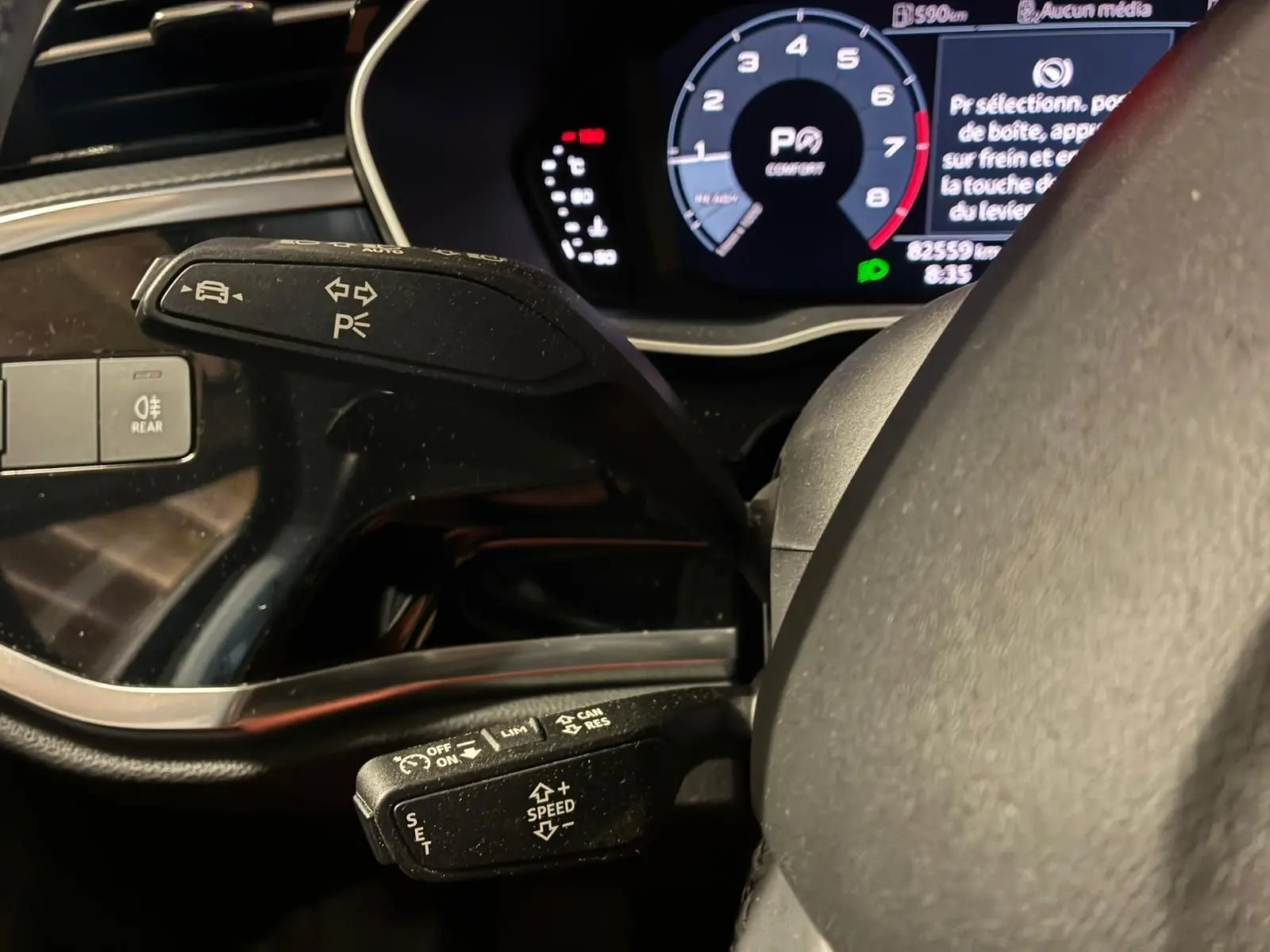 Gros plan sur les commandes au volant d’un Audi Q3 Sportback noir, avec tableau de bord numérique allumé.