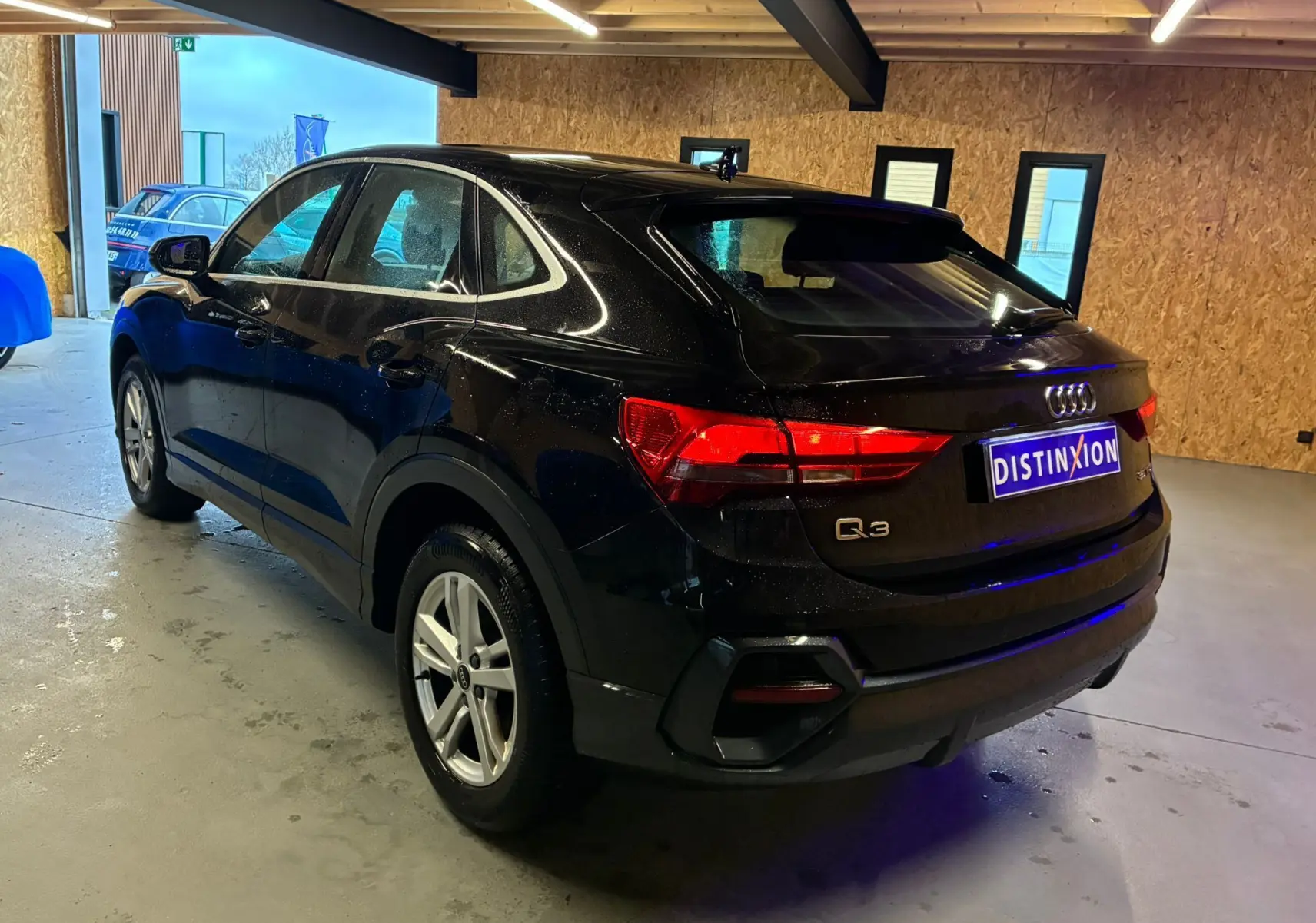 Audi Q3 Sportback noir vue 3/4 arrière droit dans un garage avec jantes alu et feux LED allumés.