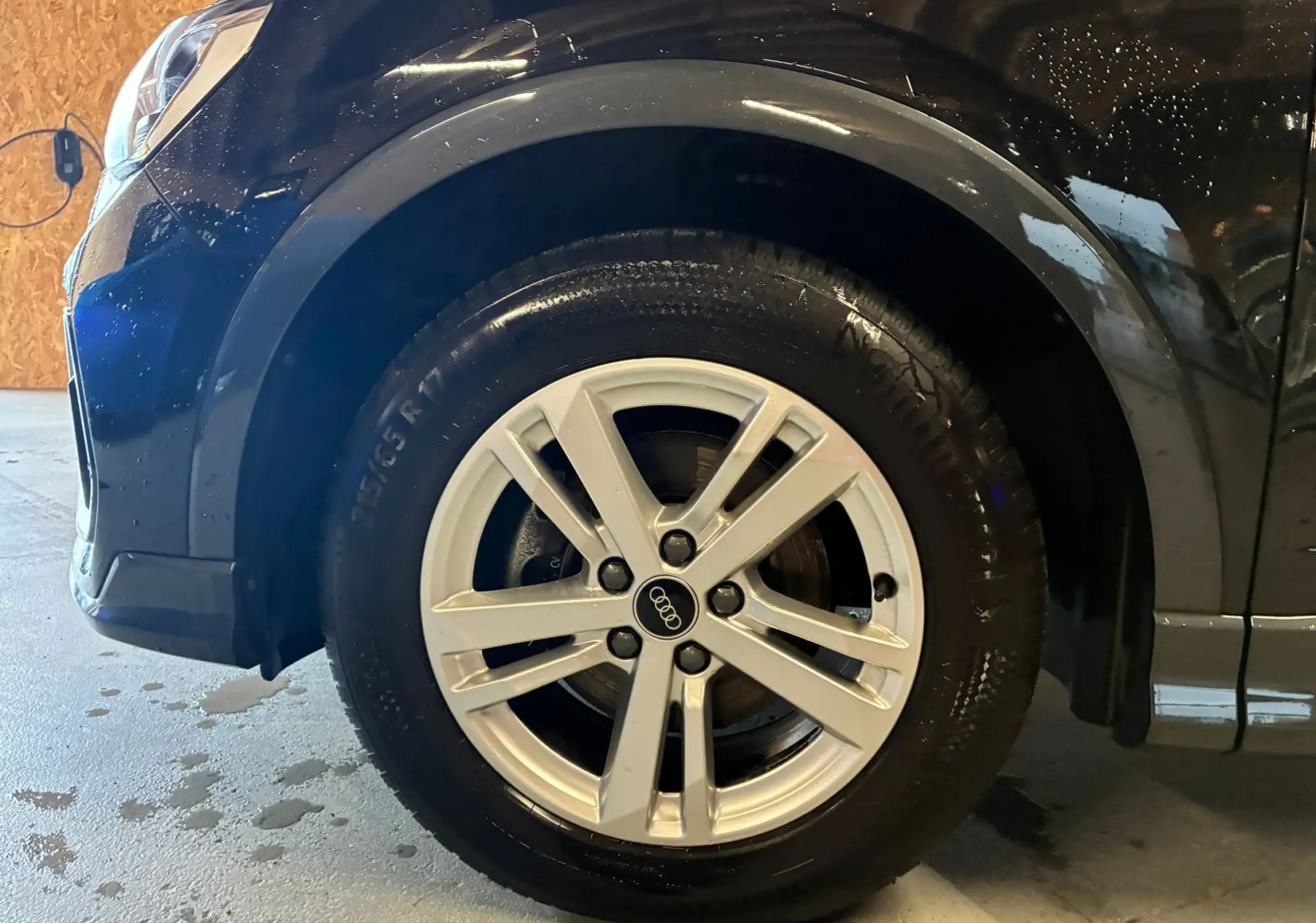 Gros plan sur la jante alu avant droite d'un Audi Q3 Sportback noir avec carrosserie brillante et mouillée.