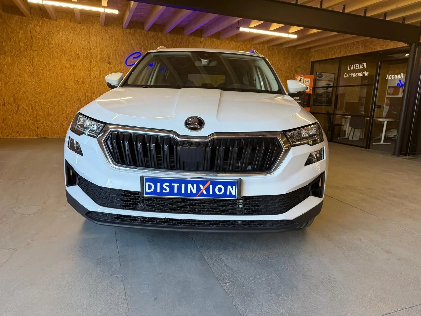 Vue frontale d'un Skoda Karoq blanc 2023 avec calandre noire et plaque Distinxion dans un garage.