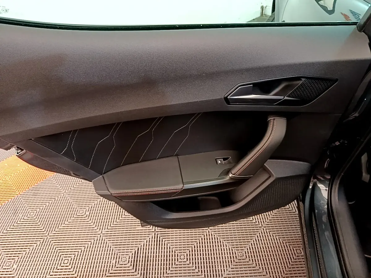 Vue rapprochée de la porte avant gauche d’une CUPRA Formentor gris foncé, avec surpiqûres rouges et poignée intégrée.