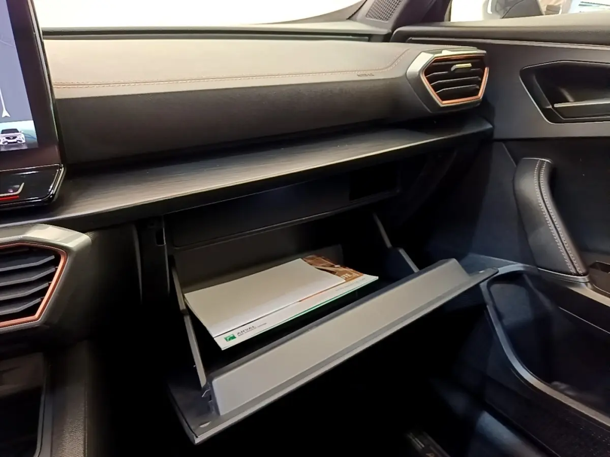 Intérieur côté passager de la CUPRA Formentor 2022, boîte à gants ouverte sous tableau de bord noir avec surpiqûres cuivre.