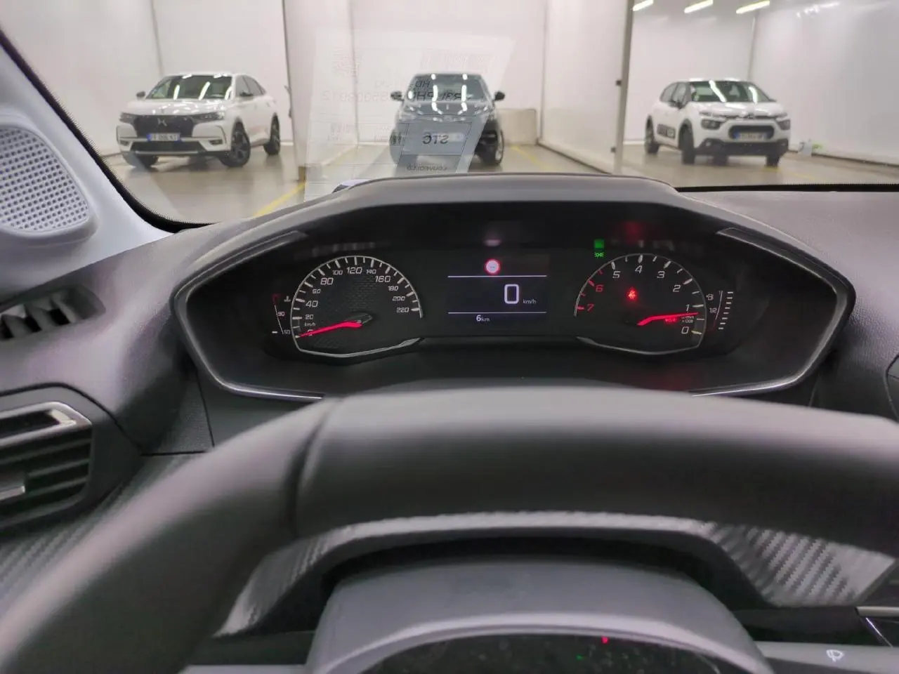 Vue depuis le poste de conduite du tableau de bord numérique de la Peugeot 208 gris clair, avec compteur et volant partiel visible.