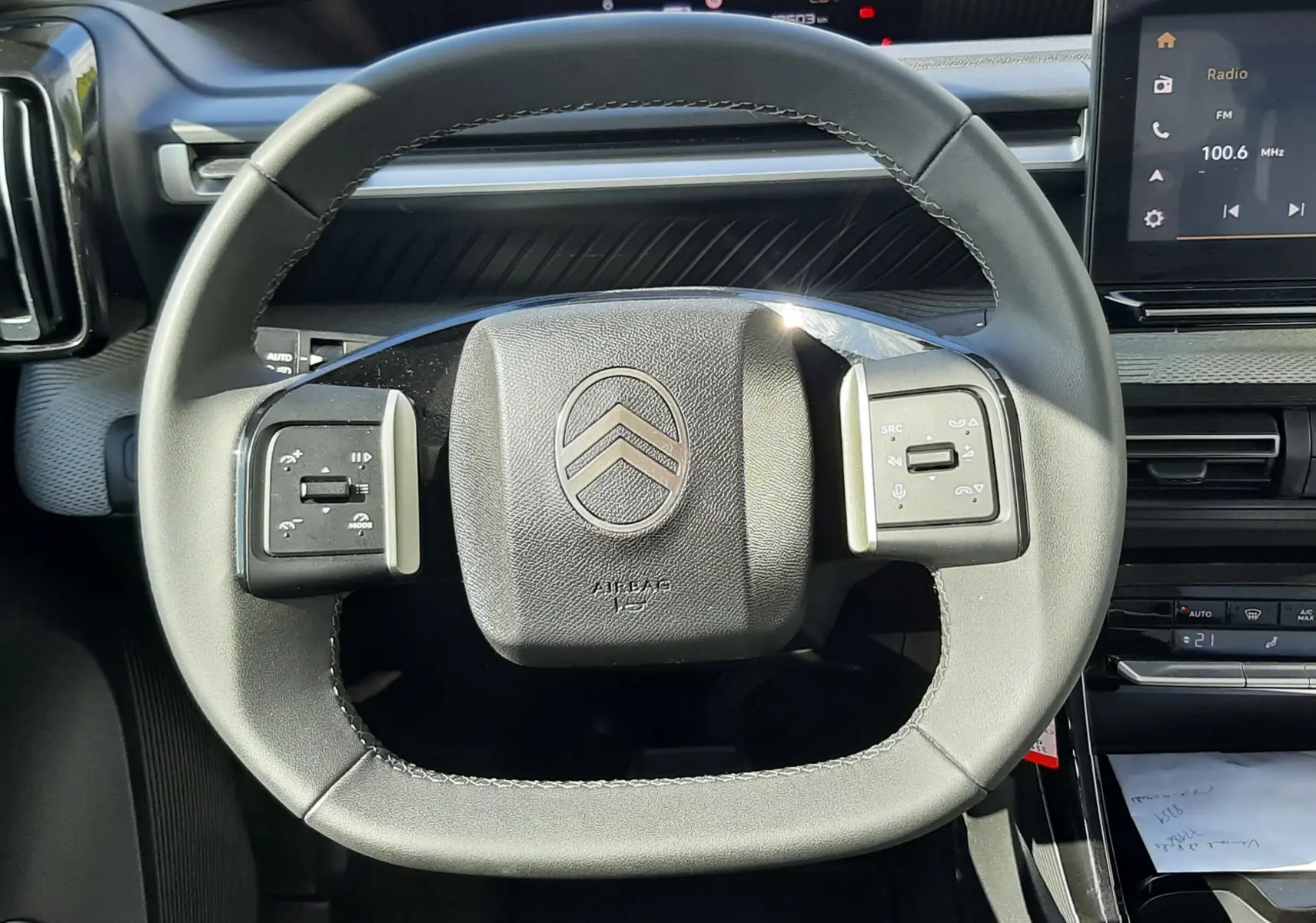 Vue rapprochée du volant noir de la Citroën C3 Aircross 2025, avec commandes intégrées et tableau de bord numérique en arrière-plan.
